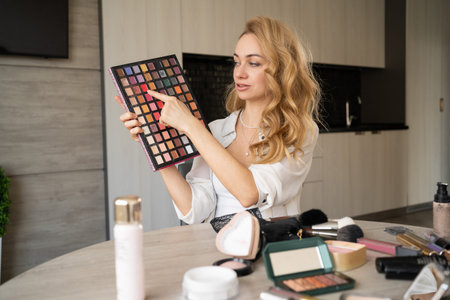 a woman blogs about make-up and beauty products. Gorgeous lady taking off makeup tutorial with makeup eyeshadow palette. Smiling girl teaches makeup using her phone. webcam viewの写真素材