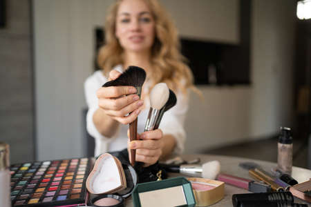 Young beautiful caucasian woman professional beauty blogger or vlogger writes makeup tutorial to share it on social media. Tells what brushes are. Online learning concept. webcam viewの写真素材