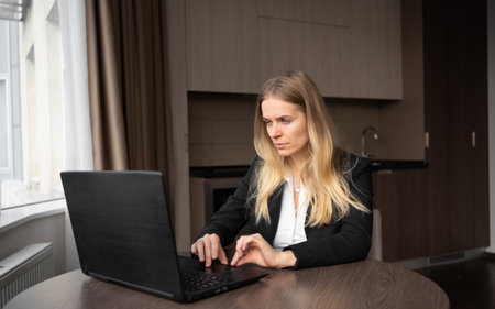 Serious freelancer woman using laptop, checking email news online, business woman sitting at home working remotely, freelancing in home officeの写真素材