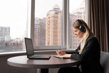 Focused millennial woman working remotely in bright cozy home office, adult student studying online, business lady video conference in headphonesの写真素材
