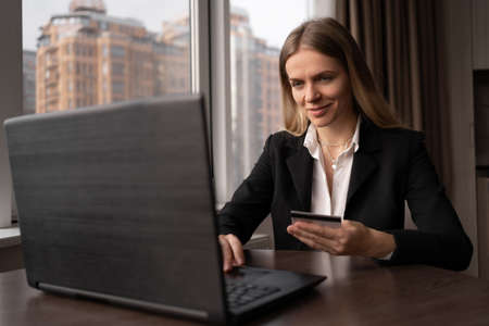 Young woman holding a credit card using a laptop, office worker shopping online, ordering goods on the internet, paying by card on the siteの写真素材
