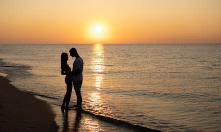A couple in love is experiencing romantic tender moments at sunset on the beach. Young lovers on summer vacation. concept of love or honeymoon. Kiss in silhouette at sunset. copy space.の写真素材