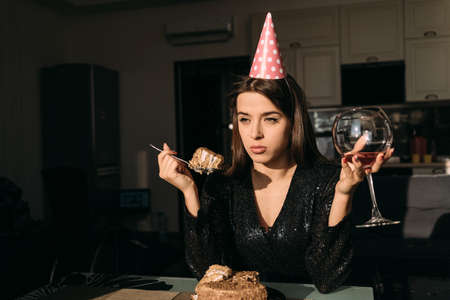 sad birthday party at home, young woman eating cake and drinking wine, celebrating anniversary alone, 25 years party, space for textの写真素材