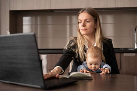 work remotely on maternity leave. A young woman with a baby in her arms is happy behind a laptop while working in the office, a happy life as a housewife. copy spaceの写真素材