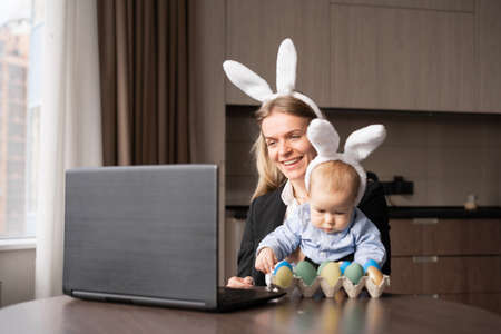 a woman and a child paint eggs for easter, make a video call using a laptop and a webcam. copyspace.の写真素材