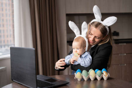 a woman and a baby paint eggs before Easter and communicate via video link with their friends. Decorated table with colorful eggs. copy spaceの写真素材