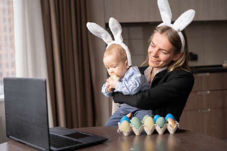 a woman and a baby paint eggs before Easter and communicate via video link with their friends. Decorated table with colorful eggs. copy spaceの写真素材