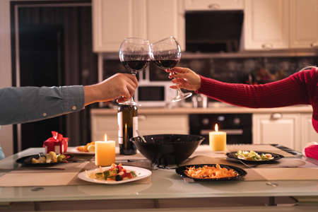 romantic dinner for two, couple with glasses of red wine in home kitchen, hands close up, date clink glasses, birthday or anniversary at home, alcoholの写真素材