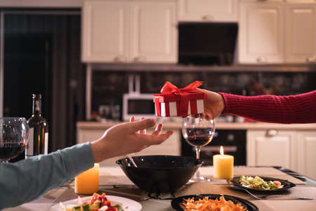 romance and gift of lovers at home in the kitchen, holding surprise gift with hands, dinner for two with wine and candles, couple no facesの写真素材