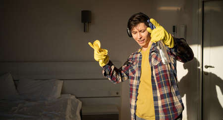 A young man listens to music with headphones and dances while cleaning the house during the day. copyspace.の写真素材
