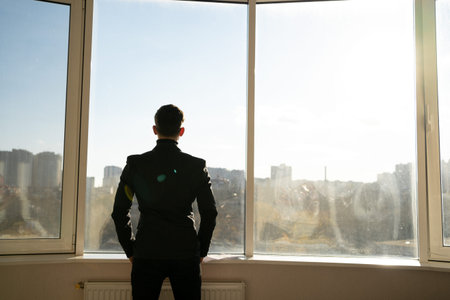 Rear view of a young successful businessman standing in the office and looking through the full...