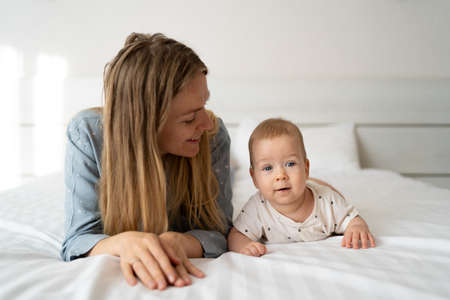 Portrait of a mother with a four month old baby in the bedroom. Young happy mum lies next to her adorable baby son, a cute blond boy playingの写真素材