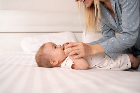 Portrait of mother and baby laughing and playing lying on bed, happy family and motherhood,...