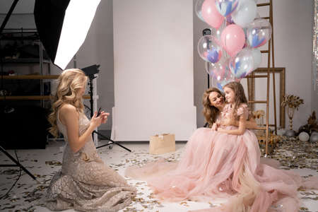 photo session on a smartphone at a professional photo studio. a woman and a child in beautiful long dresses pose for a mobile photographer. photo session of mother and daughter.の写真素材