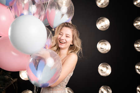 Happy girl with balloons. Happy young girl standing in dress with birthday balloons black background laughing merrily emotion of joy and delight. Banner.の写真素材