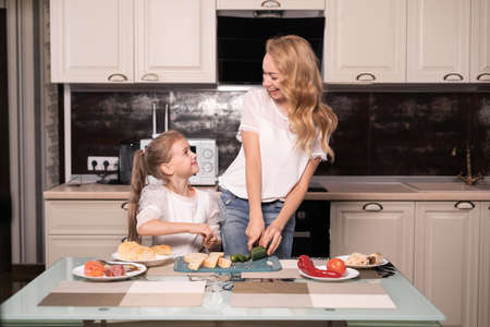 a woman and a child are preparing sandwiches at home together. Mom cuts cucumbers and daughter helps her. joint cooking. copyspace.の写真素材