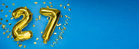 golden foil balloon number twenty seven. Birthday or anniversary card with the inscription 27. blue concrete background. Anniversary celebration. Banner. copy spaceの写真素材