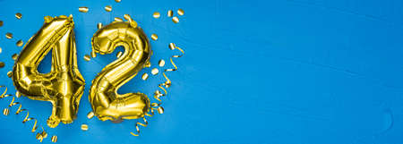 gold foil balloon number forty two. Birthday or anniversary card with the inscription 42. blue concrete background. Anniversary celebration. Banner. copy spaceの写真素材