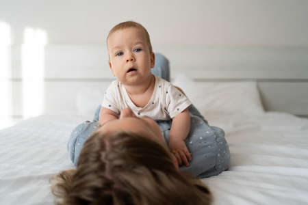 Happy family in the bedroom. young mother holding her newborn little son on her stomach while lying on the bed, copy space, happy motherhood conceptの写真素材