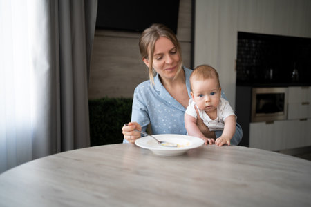 caucasian mother 30s with baby eats corn flakes with milk, parent with toddler child eat morning meal, happy motherhood, nursing diet foodの写真素材