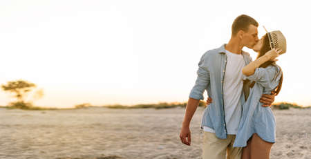 Young couple in love outdoors. Stunning sensual portrait of a young stylish fashion couple, man and woman kissing while walking along the ocean shore at sunset in the evening. copy spaceの写真素材