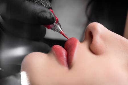 lip tattoo in a beauty salon, the process of applying coloring pigment to the lips, permanent lip makeup, female beautyの写真素材