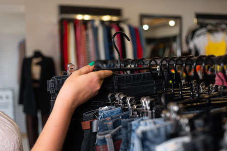 female hand sorting through hangers with jeans in a store, women's clothing on racks, a choice of trousers in a boutique, a new collection of jeansの写真素材