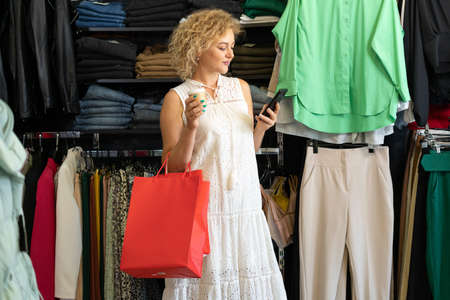 Shopping in a clothing store. Happy blonde woman with a shopping bag with things on sale. Consumerism, shopping, lifestyle conceptの写真素材