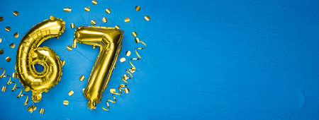 golden yellow foil balloon on blue concrete background number sixty seven. Birthday or anniversary card with the inscription 67. Anniversary celebration. Banner.の写真素材
