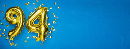 golden yellow foil balloon on blue concrete background number ninety four. Birthday or anniversary card with 94 inscription. Anniversary celebration. Banner.の写真素材