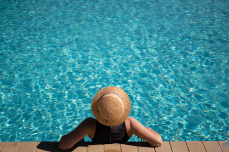 young beautiful unrecognizable woman in a straw hat is resting during a vacation in the pool. copyspace.の写真素材