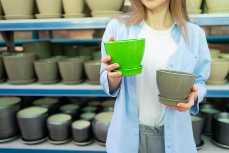 Beautiful woman in the garden center chooses ceramic pots for transplanting indoor plants at...