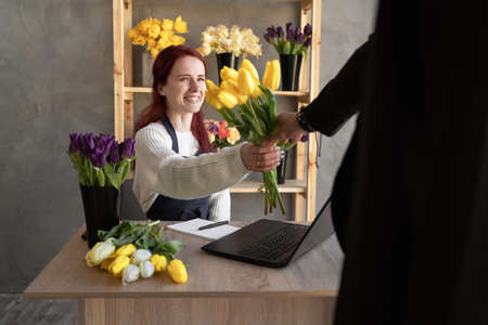 A young man buys a beautiful bouquet of tulip flowers for a girl's holiday in a cozy flower shop. Floristics and making bouquets in a flower shop. small business. happy seller. banner copy space.の写真素材
