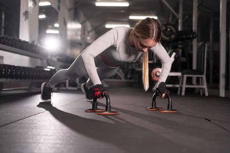 Close-up of a beautiful fitness girl in a sports top doing push-ups. She works out in the gym.の写真素材