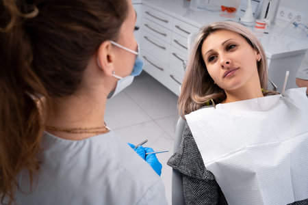 Young woman having a toothache, sitting in a dental chair at the clinic. Female patient with...