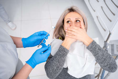 Fear dentist or fear of the doctor. Frightened and nervous patient woman in the hospital. Upset lady with phobia having panic attack in clinic before medical operation. close your mouth with your handの写真素材