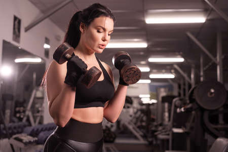 Determined woman losing weight and exercising with dumbbells. The concept of sports and recreation. Beautiful lady in sportswear with big dumbbells in her hands.の写真素材