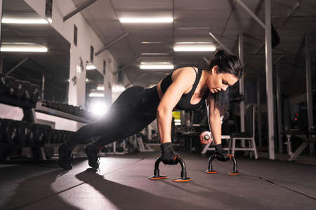 side view of a beautiful athletic girl, dressed in a black sports top and tights, does push-ups during an intensive workout in the gym. Healthy lifestyle, gymnastics concept,の写真素材