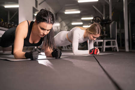 fitness, people and healthy lifestyle concept two woman in training doing plank exercises in the gym.の写真素材