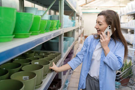 Beautiful woman in the garden center chooses ceramic pots for transplanting indoor plants at home.Gardening, planting and shopping concept.の写真素材