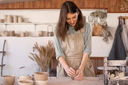 Master of art ceramics at work happy woman in an apron works in a ceramic workshop. The craftswoman creates handmade dishes in the workshop.の写真素材