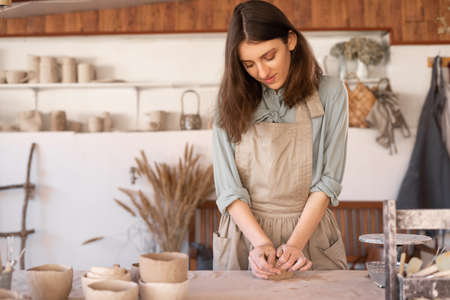 Master of art ceramics at work happy woman in an apron works in a ceramic workshop. The craftswoman creates handmade dishes in the workshop. Sの写真素材