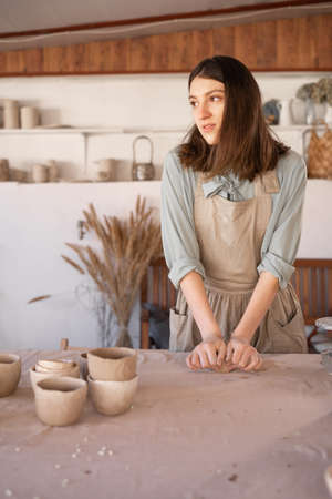 Master of art ceramics at work happy woman in an apron works in a ceramic workshop. The craftswoman creates handmade dishes in the workshop. The concept of skill and entrepreneurship.の写真素材