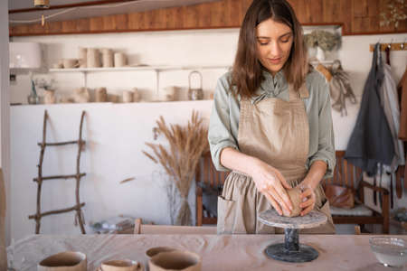 caucasian female potter working with clay on a potters wheel in a creative professional studio, Female artist creating handmade craft pottery. Relax in the handicraft workshop conceptの写真素材