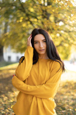 Beautiful woman in an orange sweater on a background of autumn foliage. Portrait of a joyful woman playing with leaves in the park in autumn.の写真素材