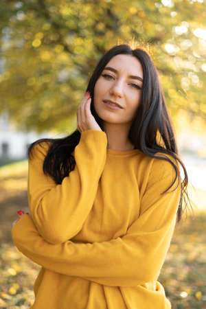 Beautiful woman in an orange sweater on a background of autumn foliage. Portrait of a joyful woman playing with leaves in the park in autumn.の写真素材