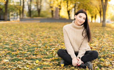 Outdoor atmospheric lifestyle photo of a young beautiful lady against the backdrop of autumn nature, the lady is sitting in a park in yellow foliage.の写真素材
