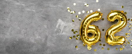 Yellow foil balloon number, number sixty two on a concrete background. Greeting card with the inscription 62. Anniversary concept. for anniversary, birthday, new year celebration. banner, copy space.の写真素材
