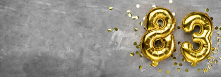 Yellow foil balloon number, number eighty three on a concrete background. Greeting card with the inscription 83. Anniversary concept. for anniversary, birthday, new year celebration. banner,の写真素材