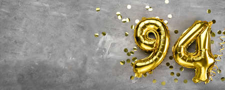 Yellow foil balloon number, number ninety-four on a concrete background. Greeting card with the inscription 94. Anniversary concept. for anniversary, birthday, new year celebration. banner,の写真素材